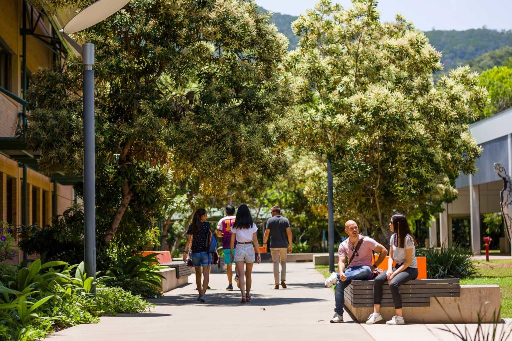 Outside on a university campus. Groups of students are walking away from the camera, two sit and talk in the foreground